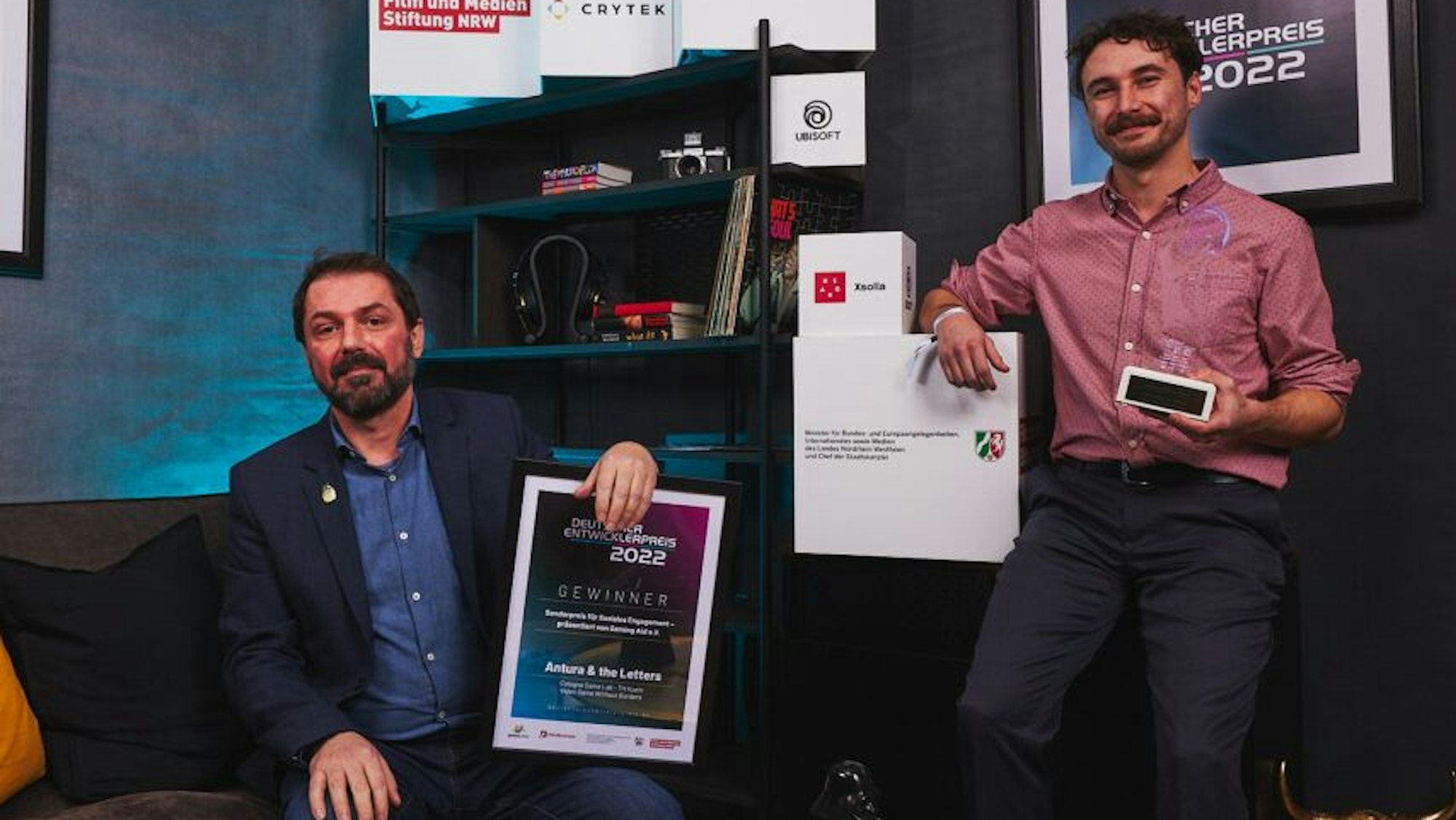 Emmanuel Guardiola, Professor am Cologne Game Lab und Mit-Initiator des Videospiels und Game Designer Chad Comeau vom Cologne Game Lab der TH Köln halten ihre Preise in der Hand.