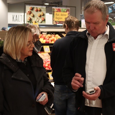 Marktmanager Achim Horbach zeigt Bürgermeisterin Sabine Preiser-Marian in der Obstabteilung des Rewe-Centers, wie die Warenscanner funktionieren, mit denen Kunden nun während des Einkaufs ihre Produkte scannen können.