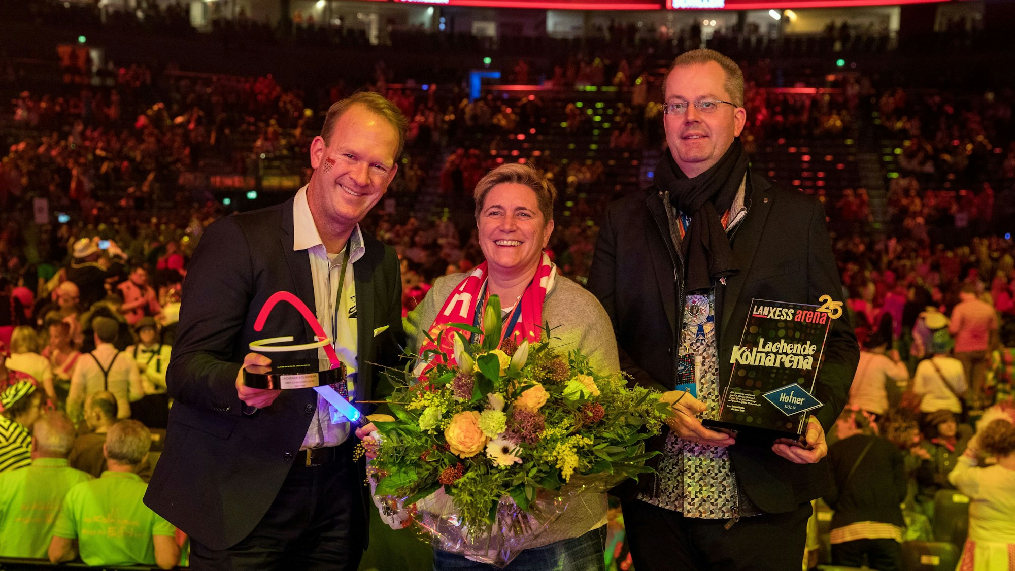 Jubiläum: Arena-Chef Stefan Löcher, Nathalie Drmota und Michael Burgmer bei der Ehrung zu 25 Jahren „Lachende Kölnarena“.