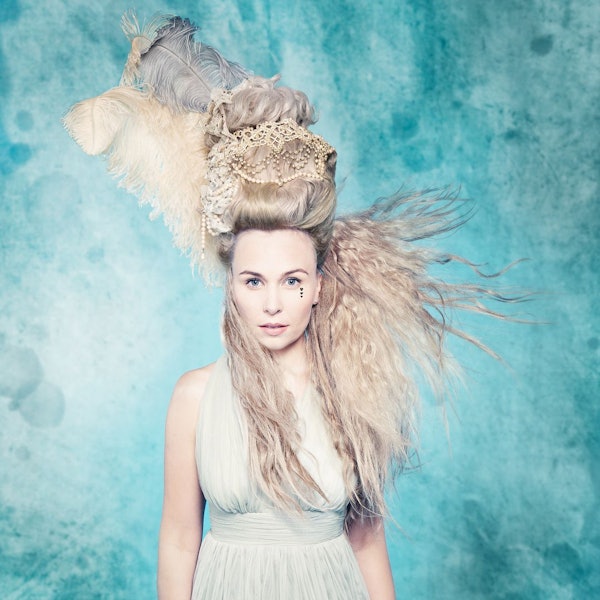 Elsa Dreisig steht mit wehenden Haaren vor einer blauen Wand.