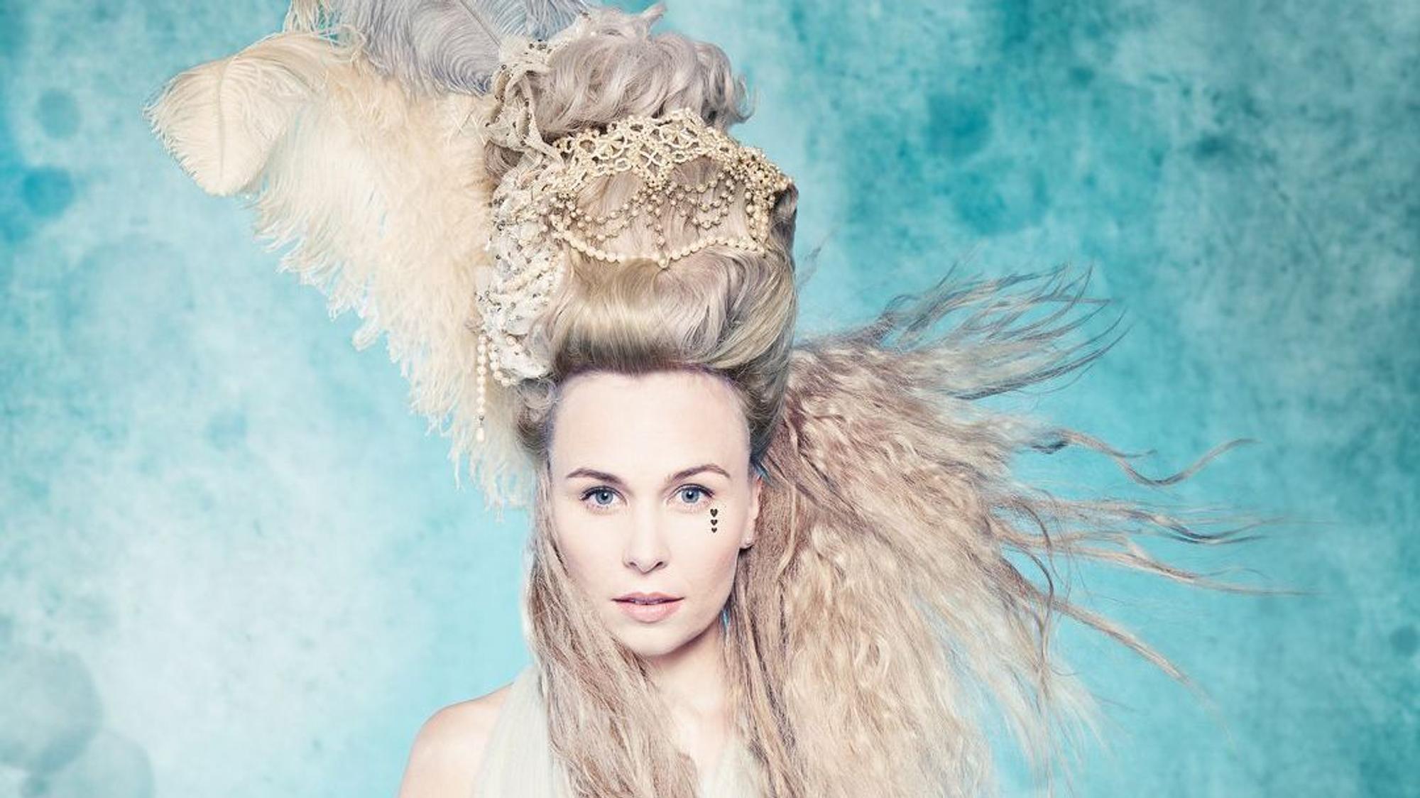 Elsa Dreisig steht mit wehenden Haaren vor einer blauen Wand.