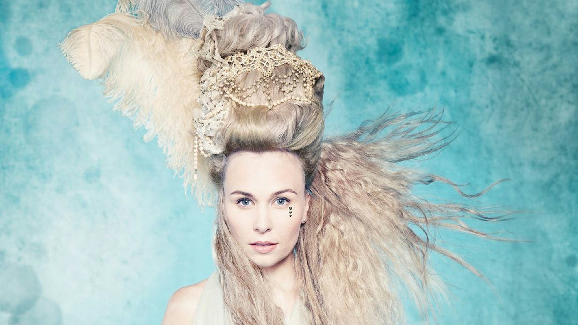 Elsa Dreisig steht mit wehenden Haaren vor einer blauen Wand.