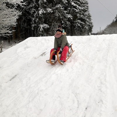 Ein Kind sitzt auf einem Schlitten und fährt einen Hügel runter.