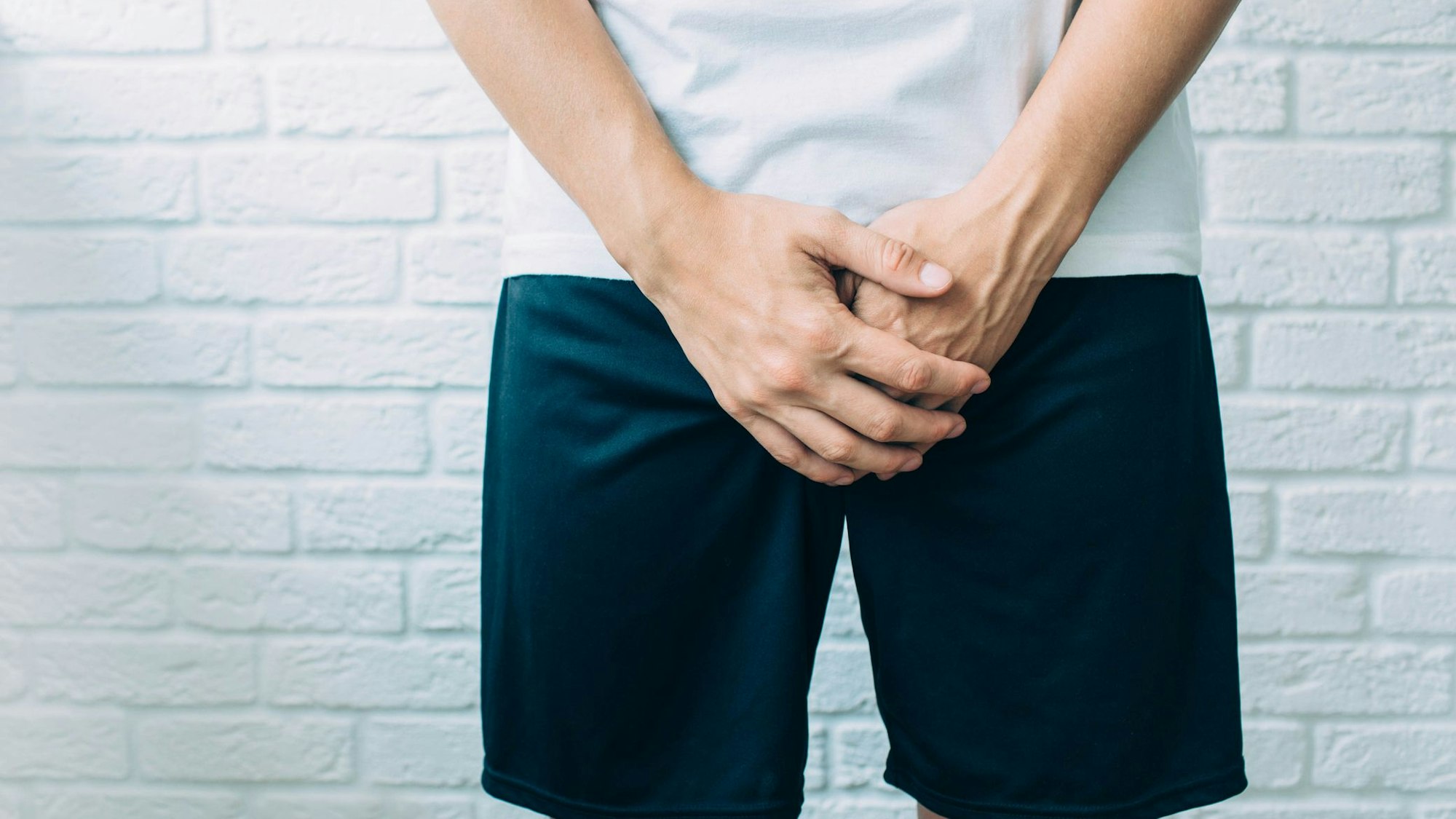 Mann hält sich die Hände vor den Schritt.