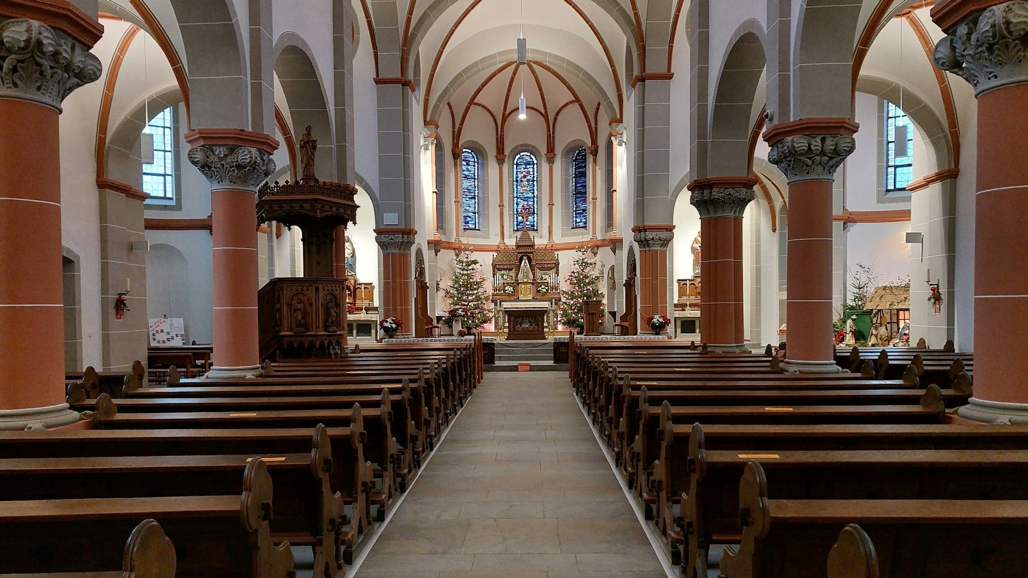 Rechts und links neben einem leeren Gang zum Altar stehen leere Kirchenbänke.