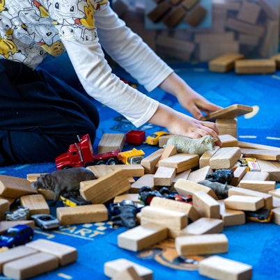 In einer Kindertagesstätte liegen Holzbauklötze, Spielzeugautos und Tierfiguren auf dem Fußboden, auf dem zwei Kinder spielen.