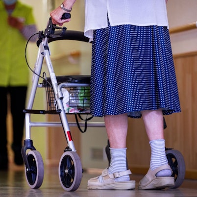 Eine Seniorin geht mit ihrem Rollator über den Gang in einer Pflegeeinrichtung.