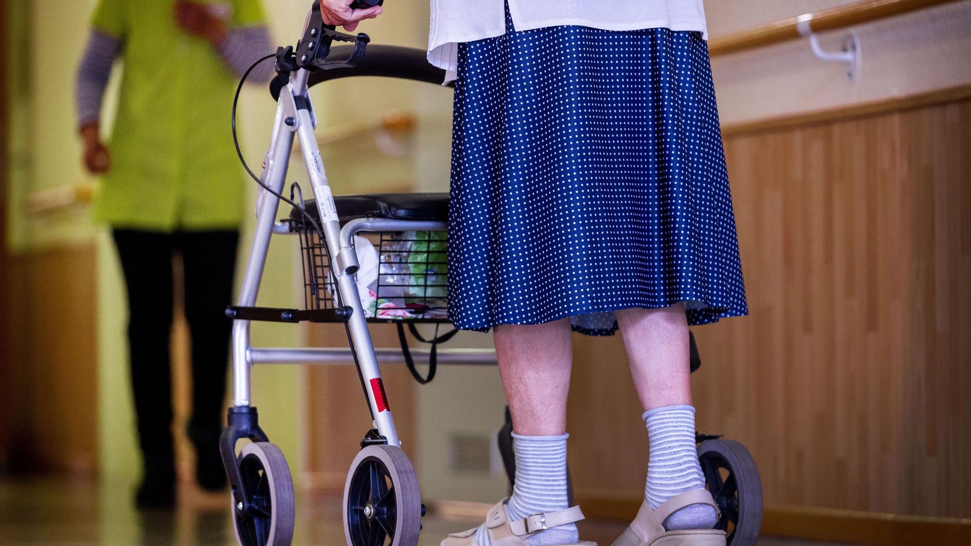 Eine Seniorin geht mit ihrem Rollator über den Gang in einer Pflegeeinrichtung.
