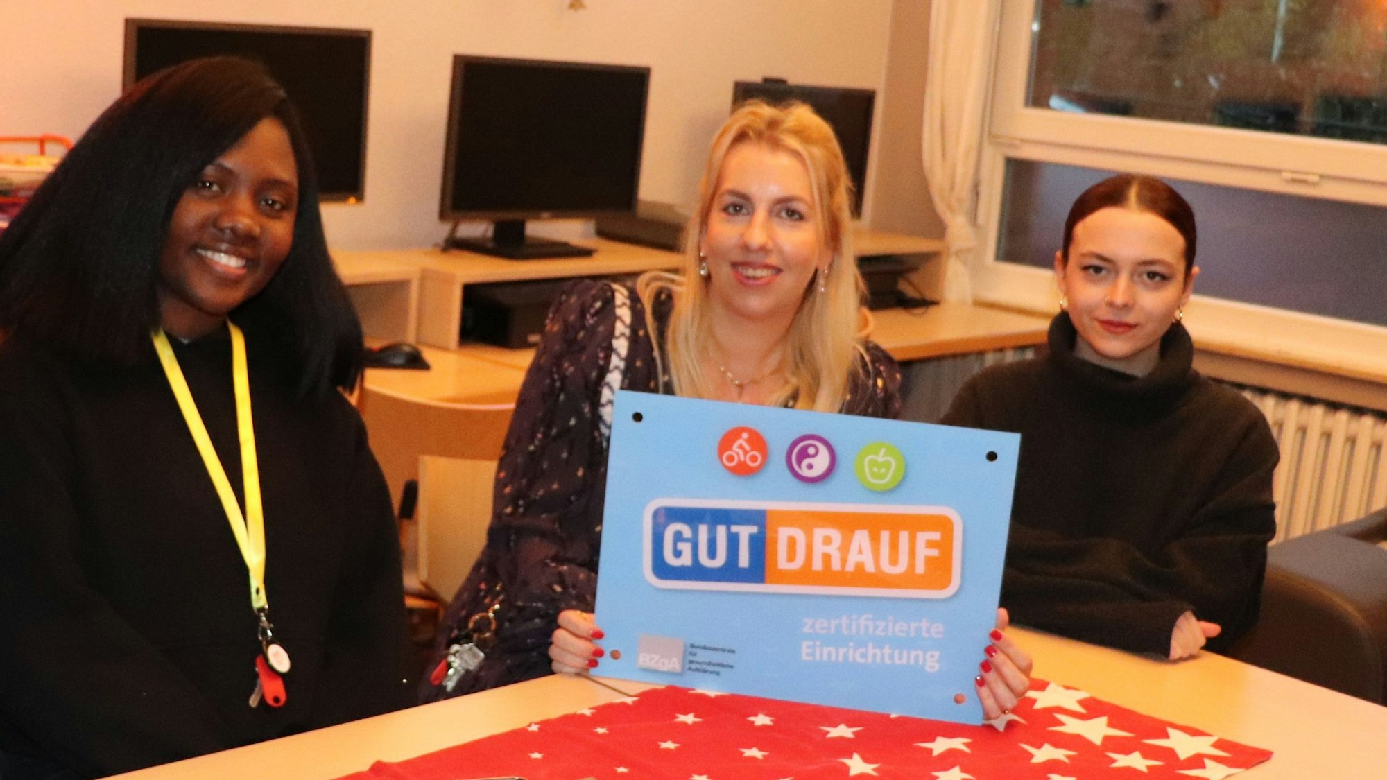 Bewohnerinnen des Mädchenheims sitzen mit der Praktikantin Liz aus Uganda und der Leiterin Nina Ryans an einem Tisch und halten das „Gut drauf“-Zertifikat in die Höhe.