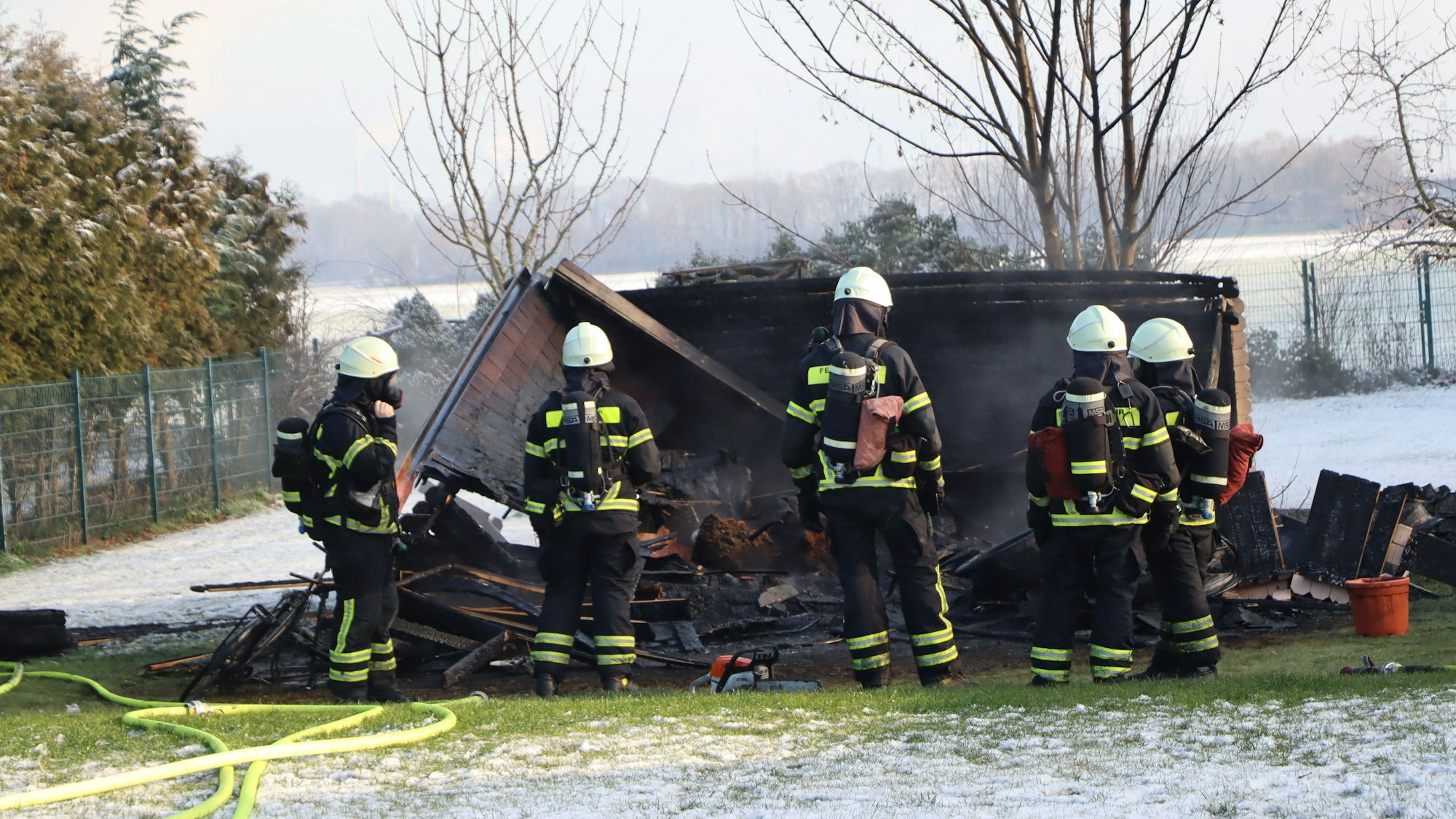 Feuerwehrleute stehen in Ausrüstung vor der eingestürzten Hütte.