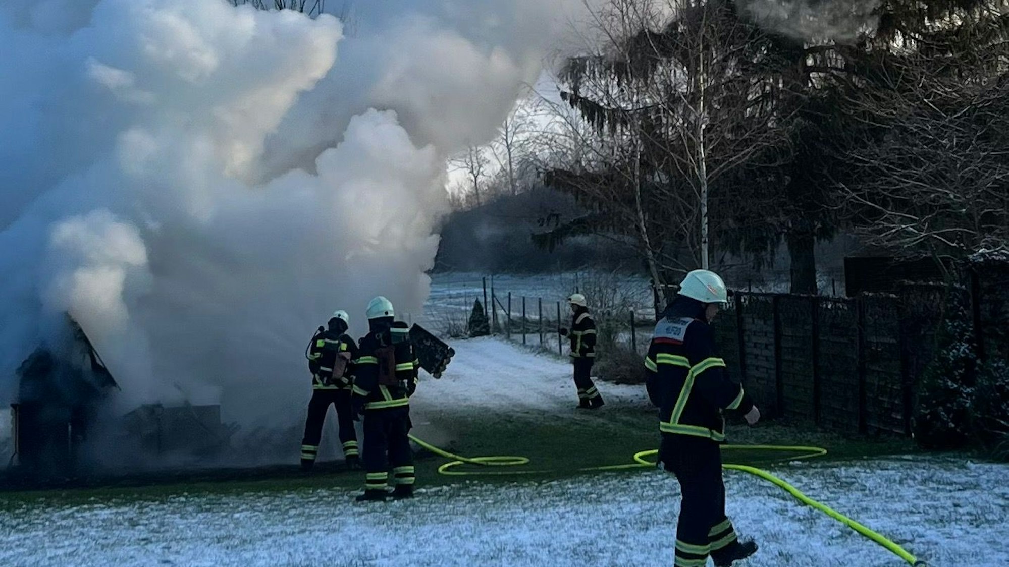 Feuerwehrleute löschen das Haus, eine Wolke aus Rauch und Dampf steigt nach oben.