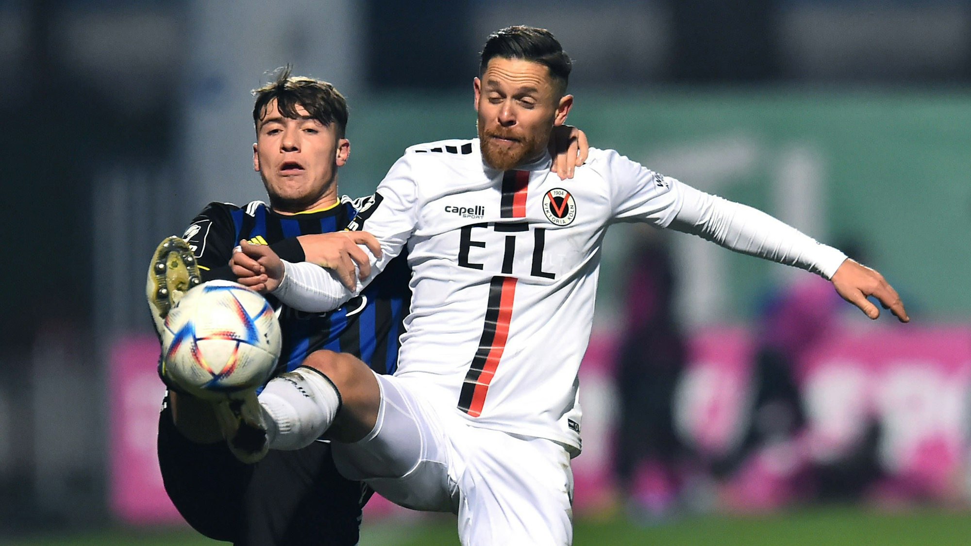 Ein Fußballspieler hält seinen Gegner im Zweikampf am Arm und an der Schulter fest.