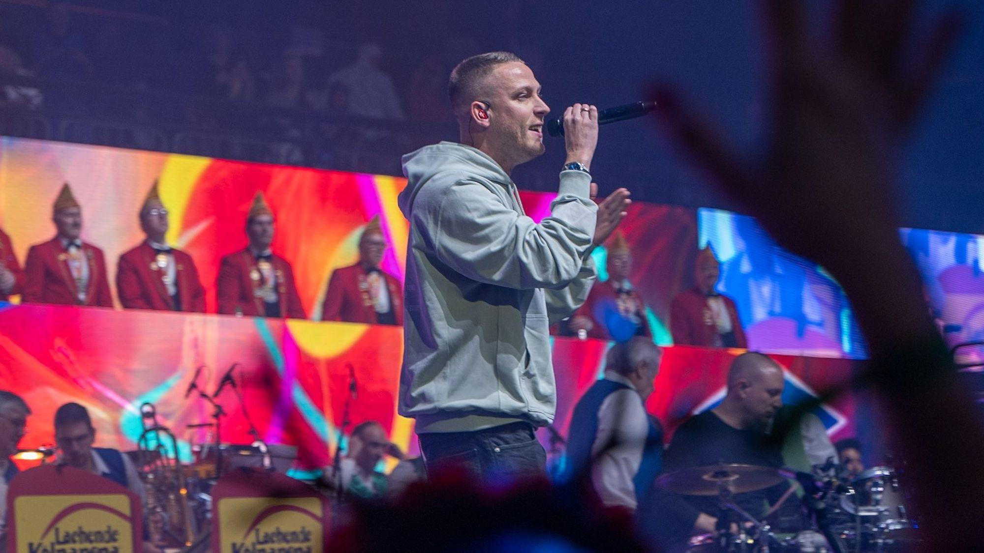 Mo-Torres bei der Lachenden Kölnarena. Er trägt einen grauen Hoodie und hält ein Mikrofon in der Hand.