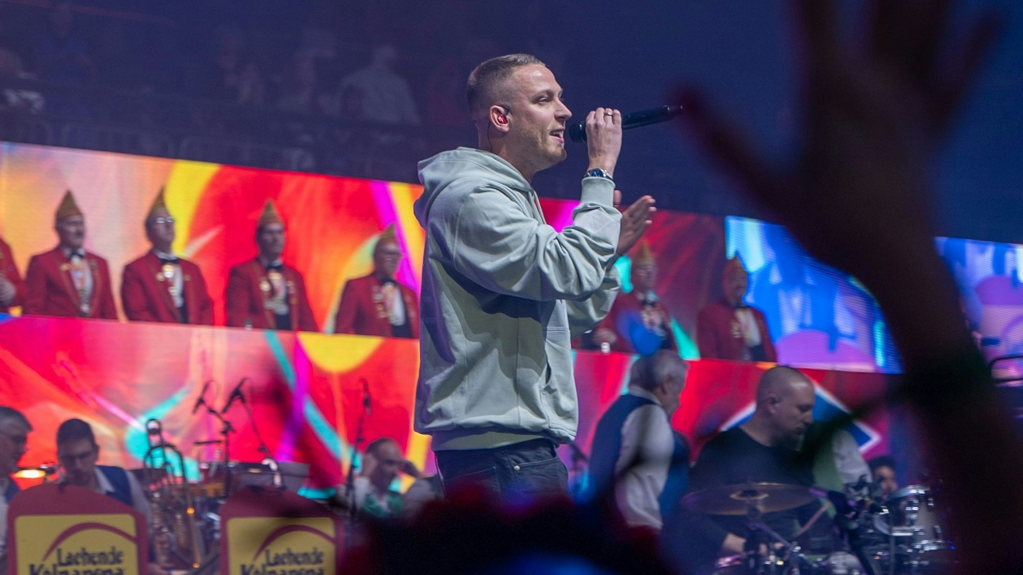 Mo-Torres bei der Lachenden Kölnarena. Er trägt einen grauen Hoodie und hält ein Mikrofon in der Hand.