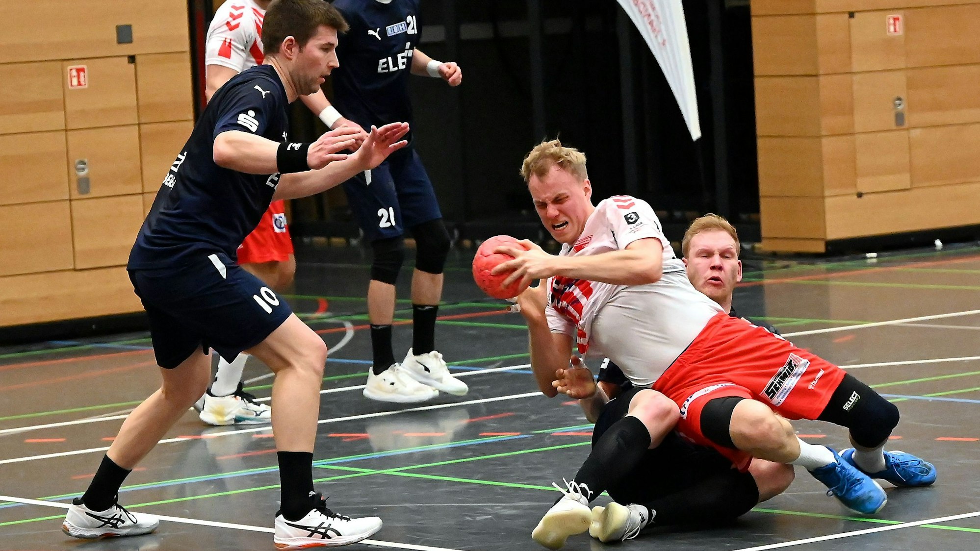 Ein Handballer wird von seinem Gegenspieler auf den Boden gezogen.