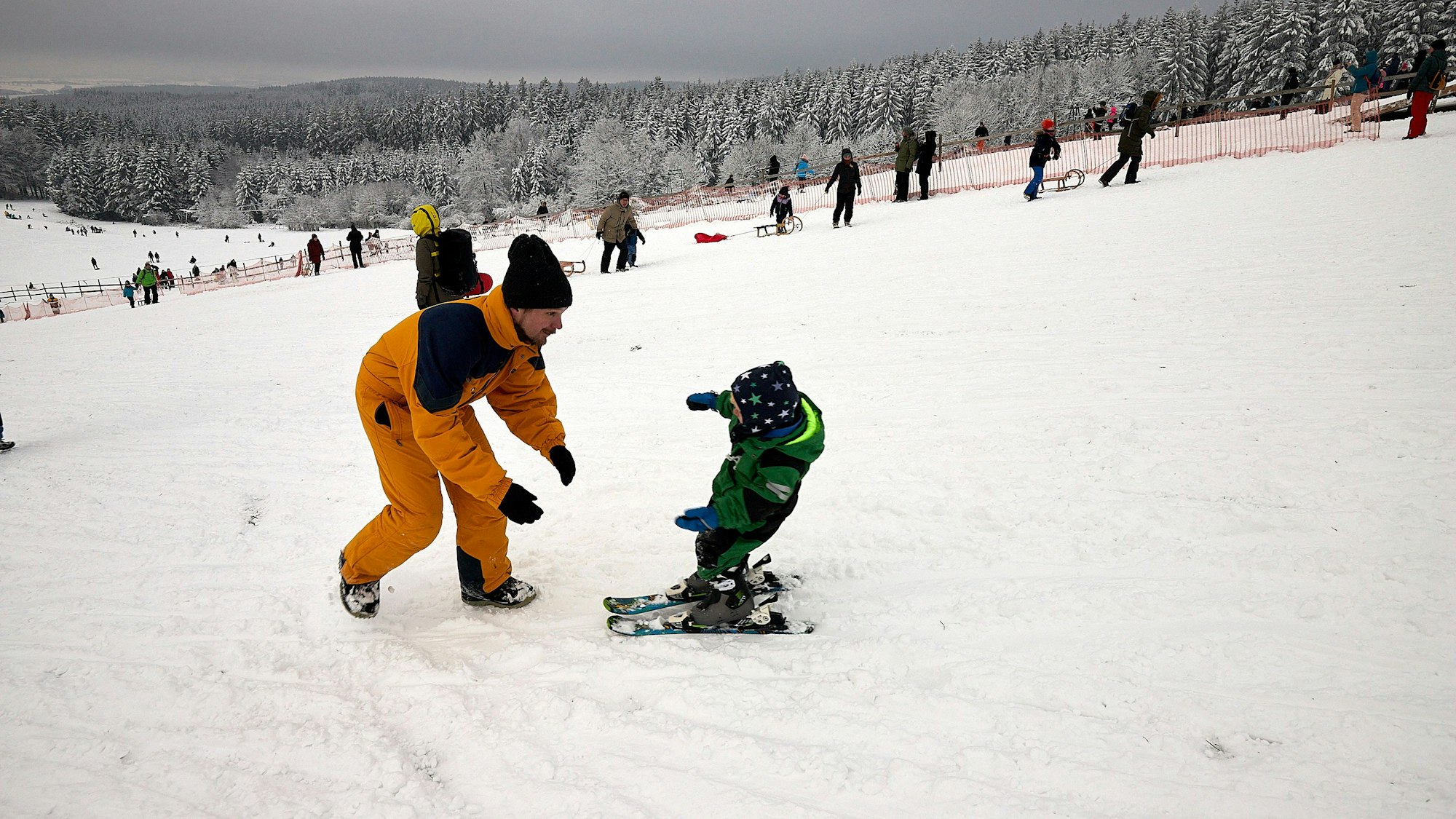 Ein Vater übt mit seinem Sohn auf einer verschneiten Ski-Piste das Ski fahren