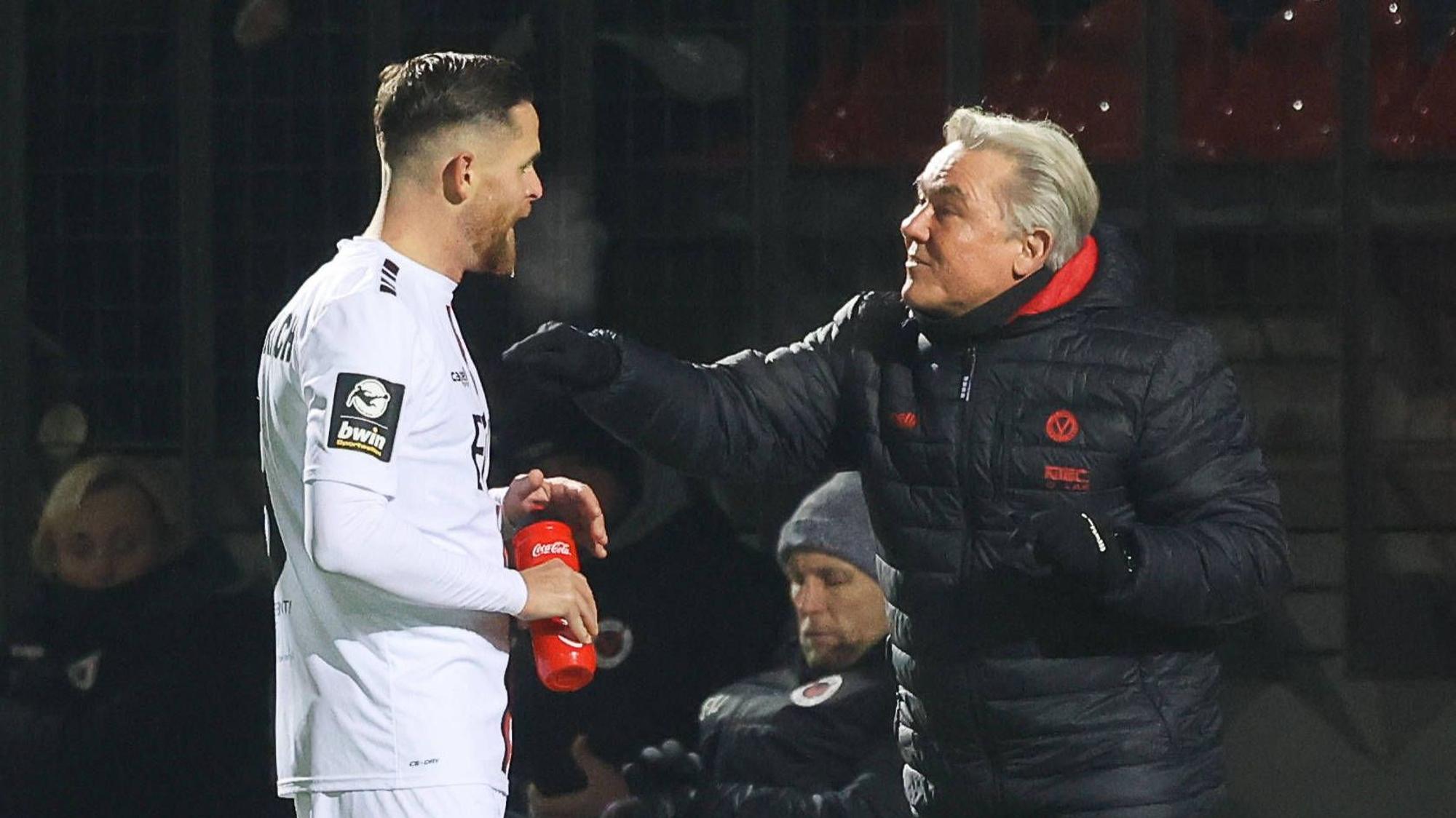 Ein Fußballtrainer redet am Spielfeldrand auf seinen Spieler ein.