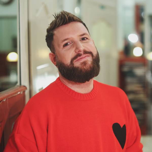 Giu im Café, er trägt einen roten Pullover mit einem Herz darauf.