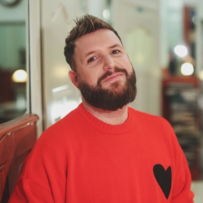 Giu im Café, er trägt einen roten Pullover mit einem Herz darauf.