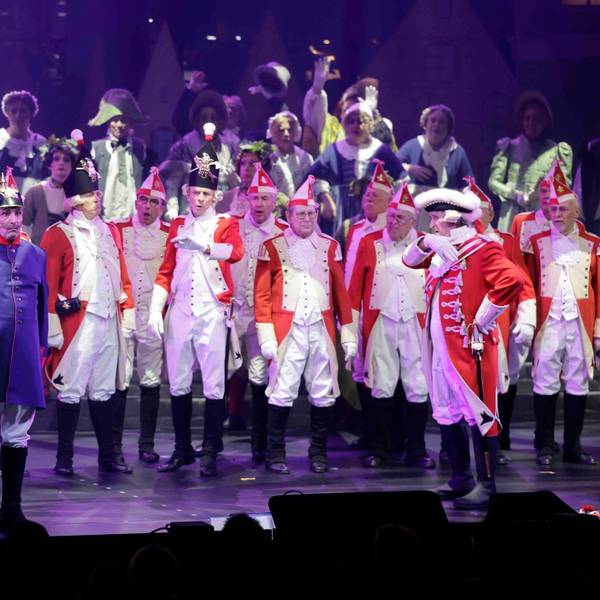Beim Diverteissementchen stehen viele Männer in rot-weißen Uniformen auf der Bühne, vorne ein "Preuße" in blau-roter Uniform.