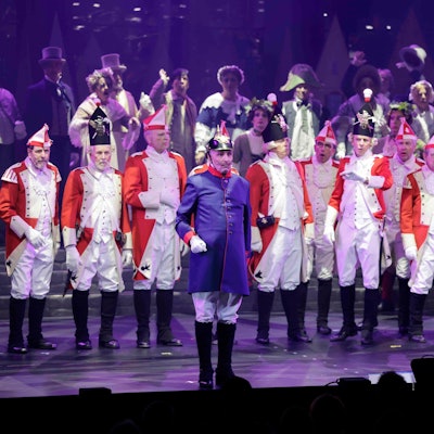 Beim Diverteissementchen stehen viele Männer in rot-weißen Uniformen auf der Bühne, vorne ein "Preuße" in blau-roter Uniform.