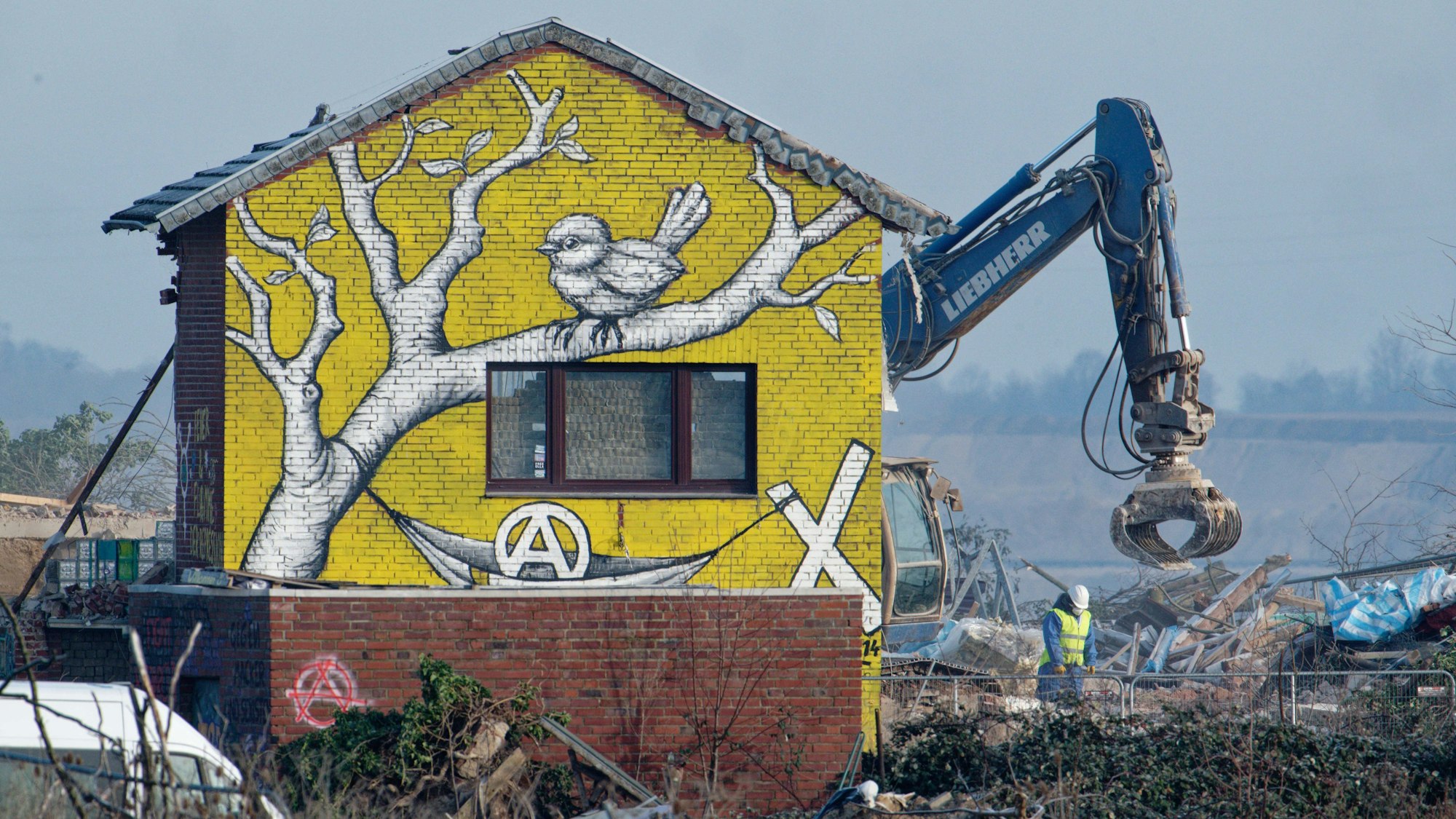 Ein Bagger reißt ein bemaltes Haus in Lützerath ab.