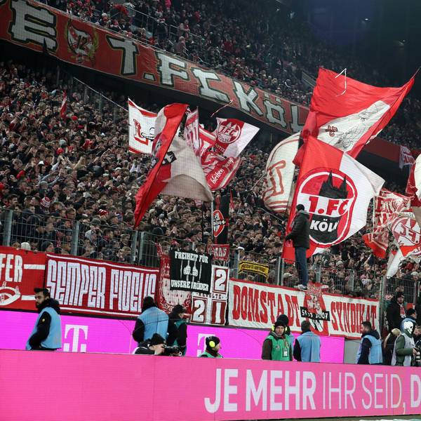 In der Südkurve des Rhein-Energie-Stadions sind mehrere Fahnen des 1. FC Köln zu sehen. Die Anhänger des Bundesligisten unterstützen ihren Verein im Rahmen eines Spiels unter Flutlicht.