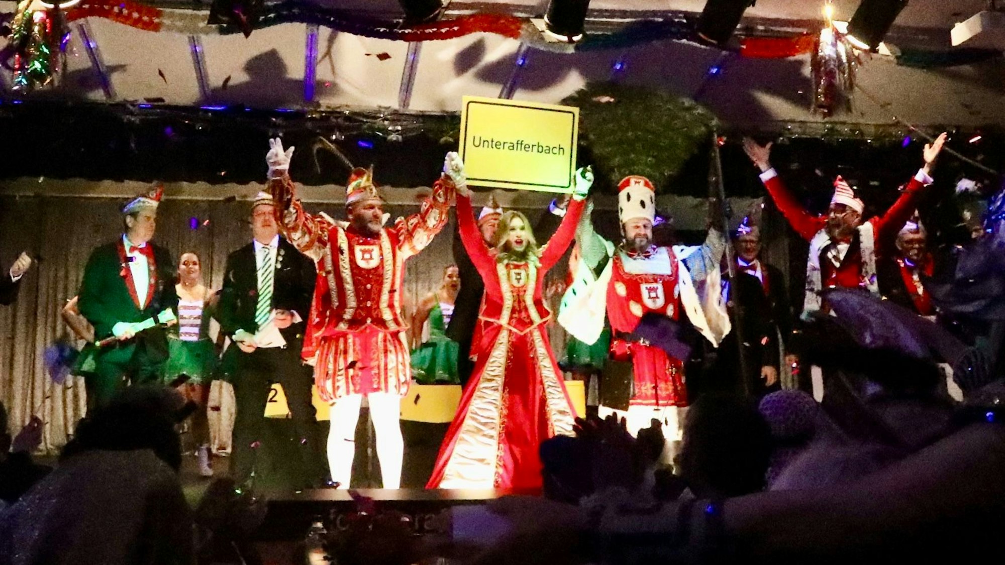 Das Porzer Dreigestirn in Unterafferbach auf der Bühne. Sie halten ein Ortsschild von Unterafferbach hoch.