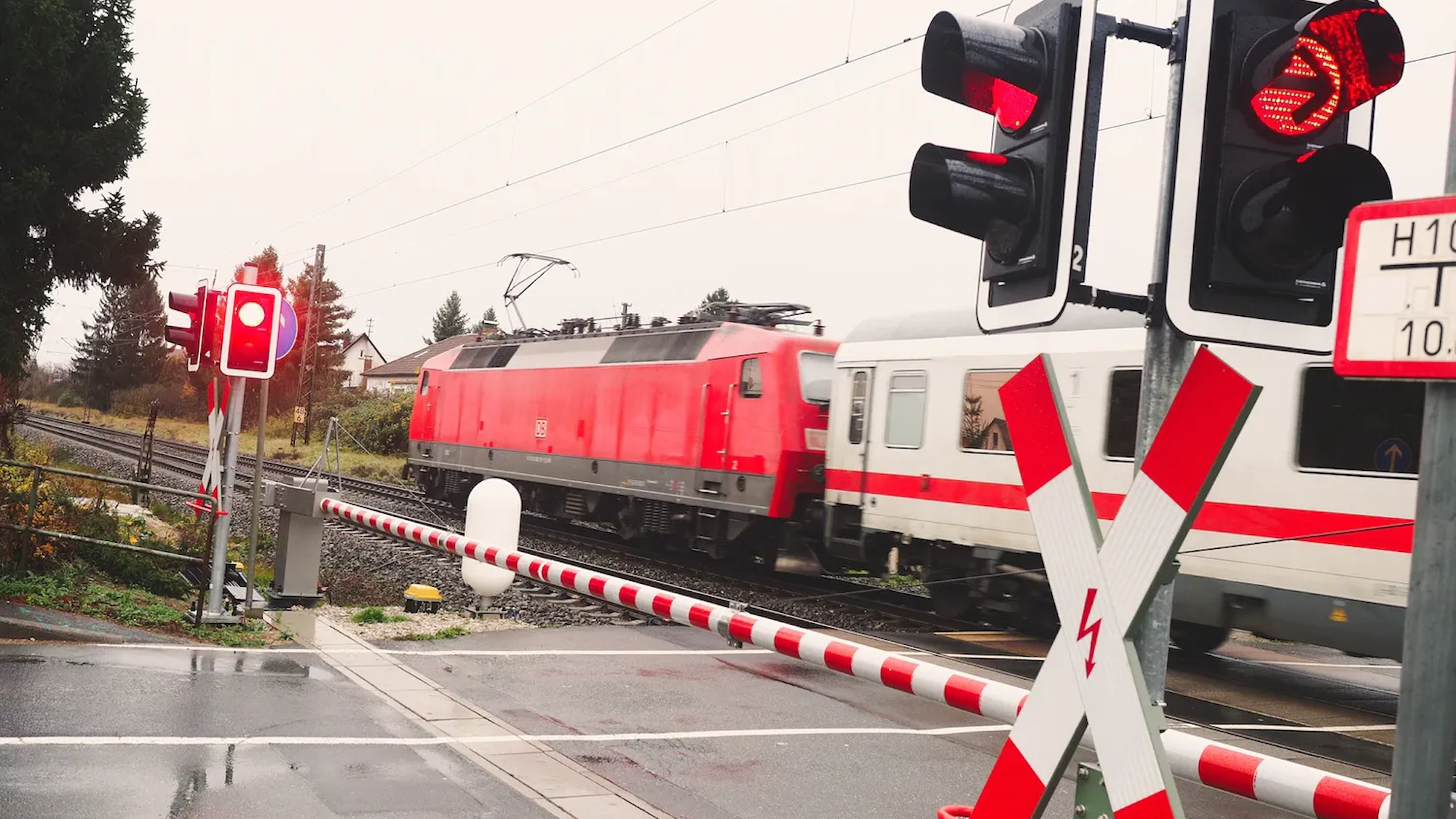 Das Foto zeigt einen Zug, der einen beschrankten Bahnübergang passiert.
