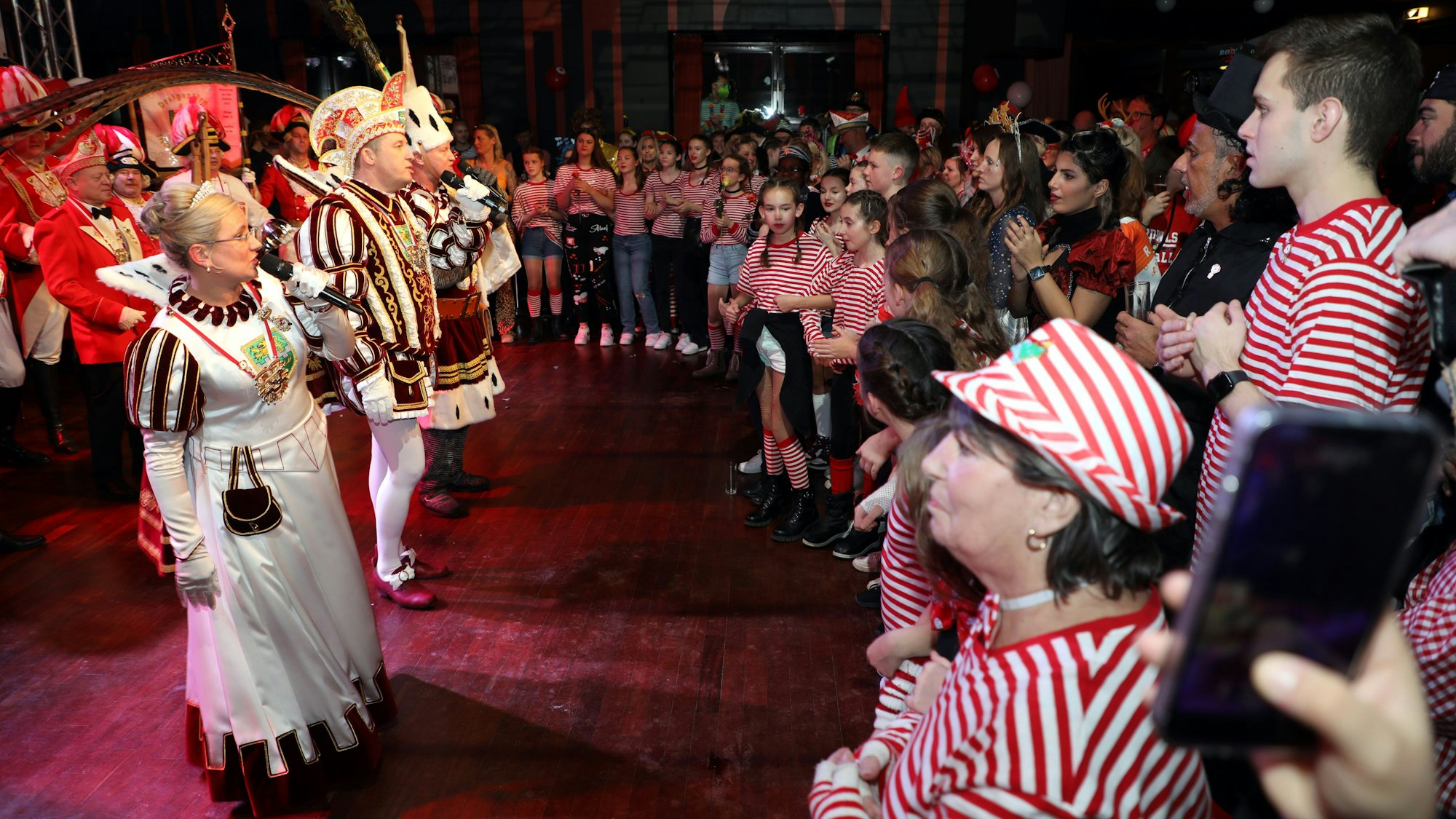Das Dreigestirn singt umringt von verkleideten Jecken.