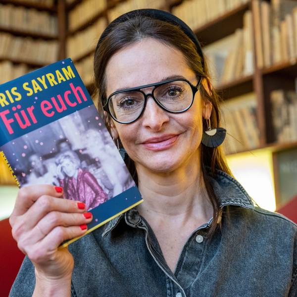 Sayram mit Bücherregalen im Hintergrund.