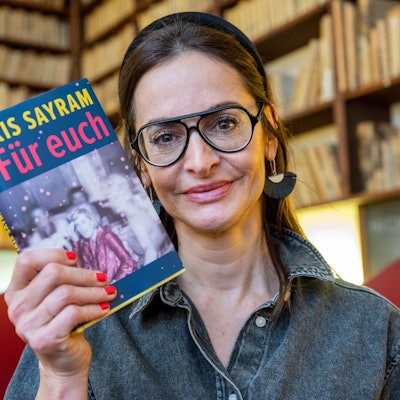 Sayram mit Bücherregalen im Hintergrund.
