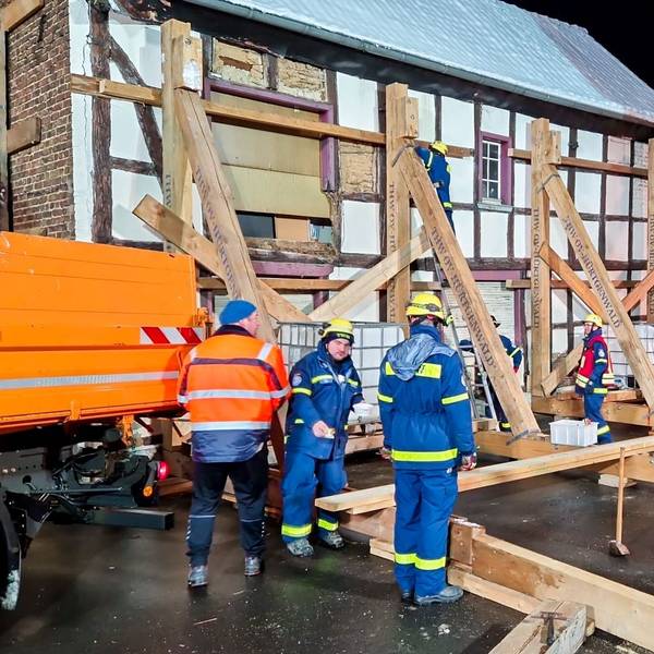 Das Foto zeigt die Einsatzstelle mit THW-Leuten, die an einem Fachwerkhaus eine Stützkonstruktion aus Holz errichtet haben.