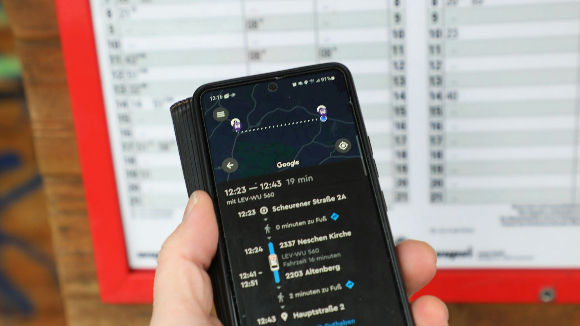 Ein Handy mit der App des Auf-Abruf-Taxis Efi ist vor einem Busfahrplan mit wenigen Verbindungen zu sehen.