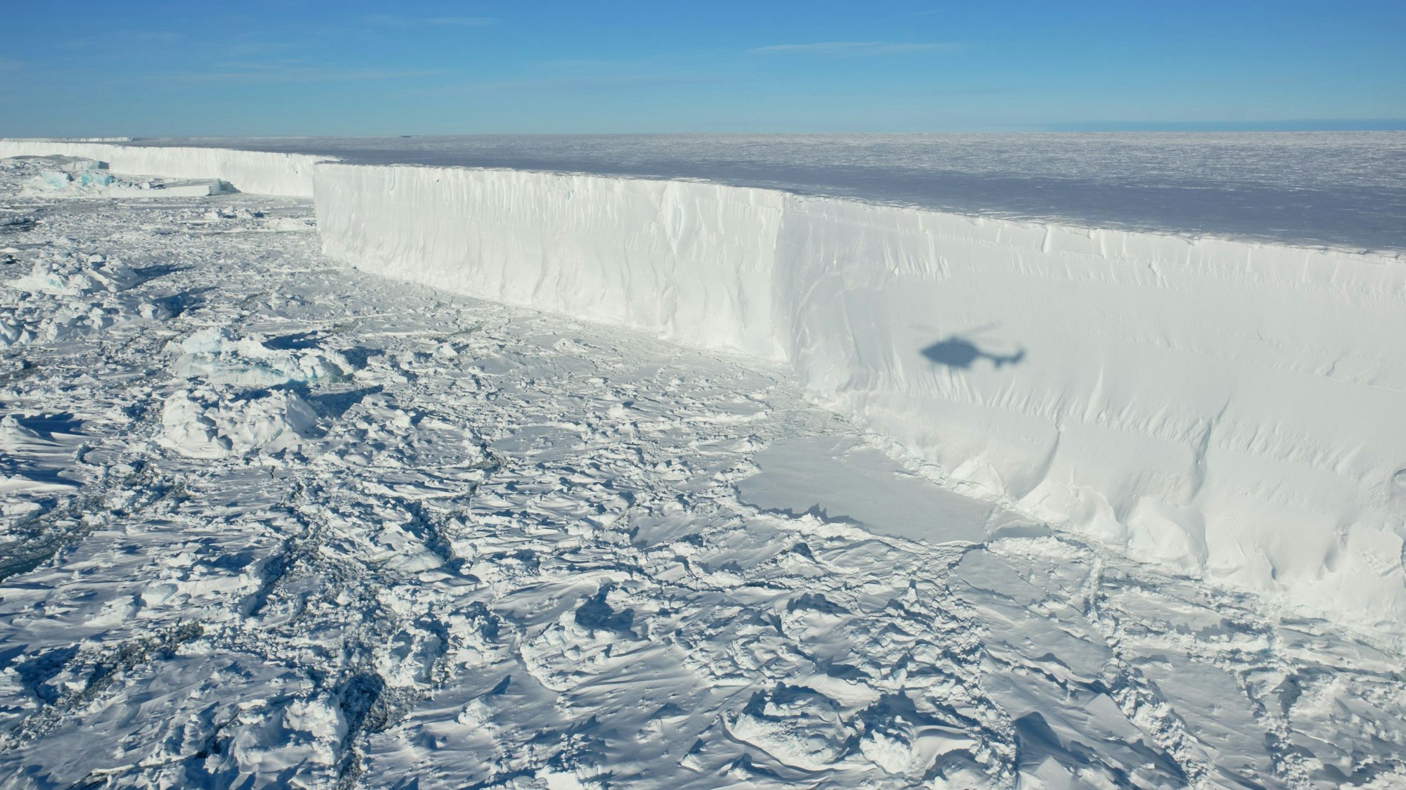 Das Foto zeigt den Eisberg A 74, der sich vom Festland löst, ein Helikopter fliegt darüber.