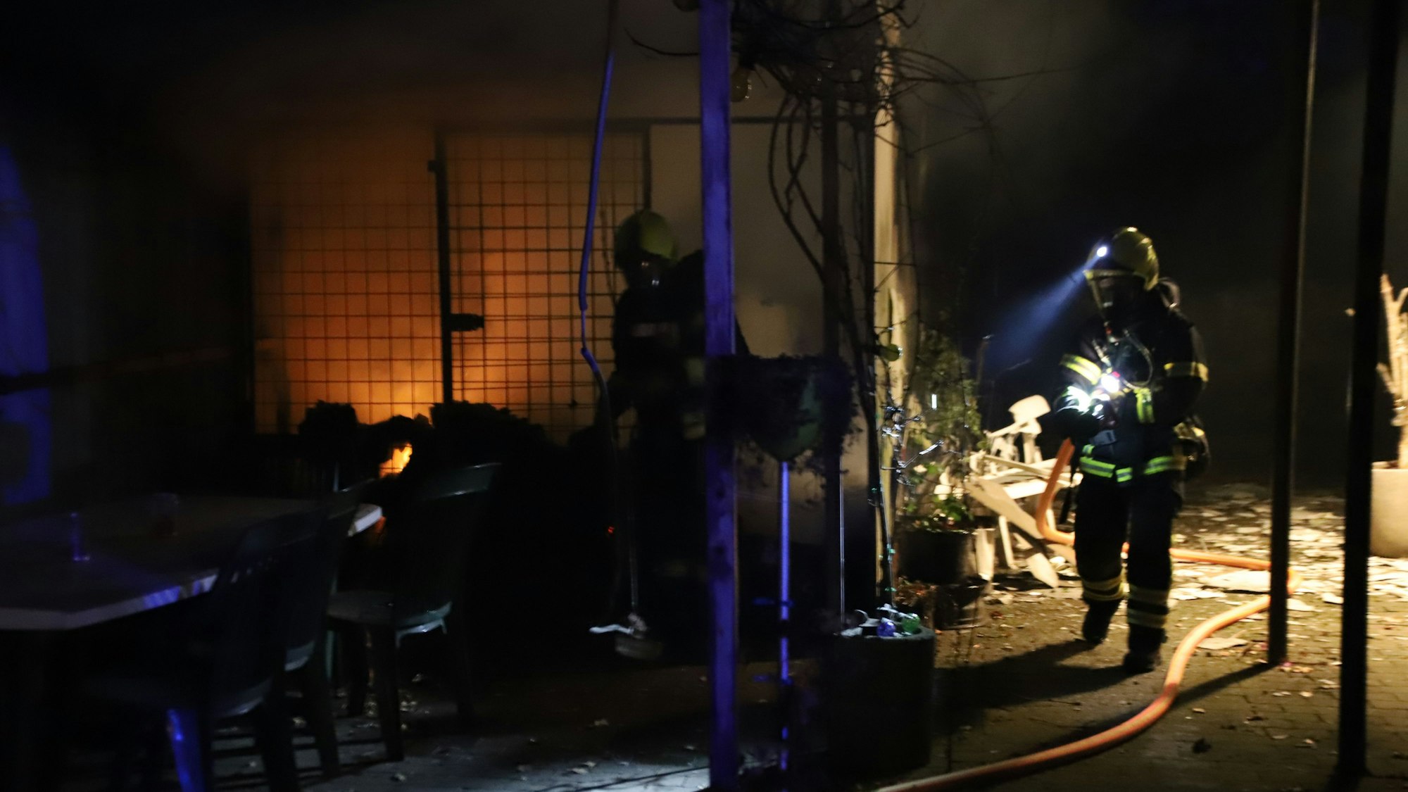 Feuerwehrleute stehen an der Gartenlaube, in der das Feuer ausgebrochen ist.