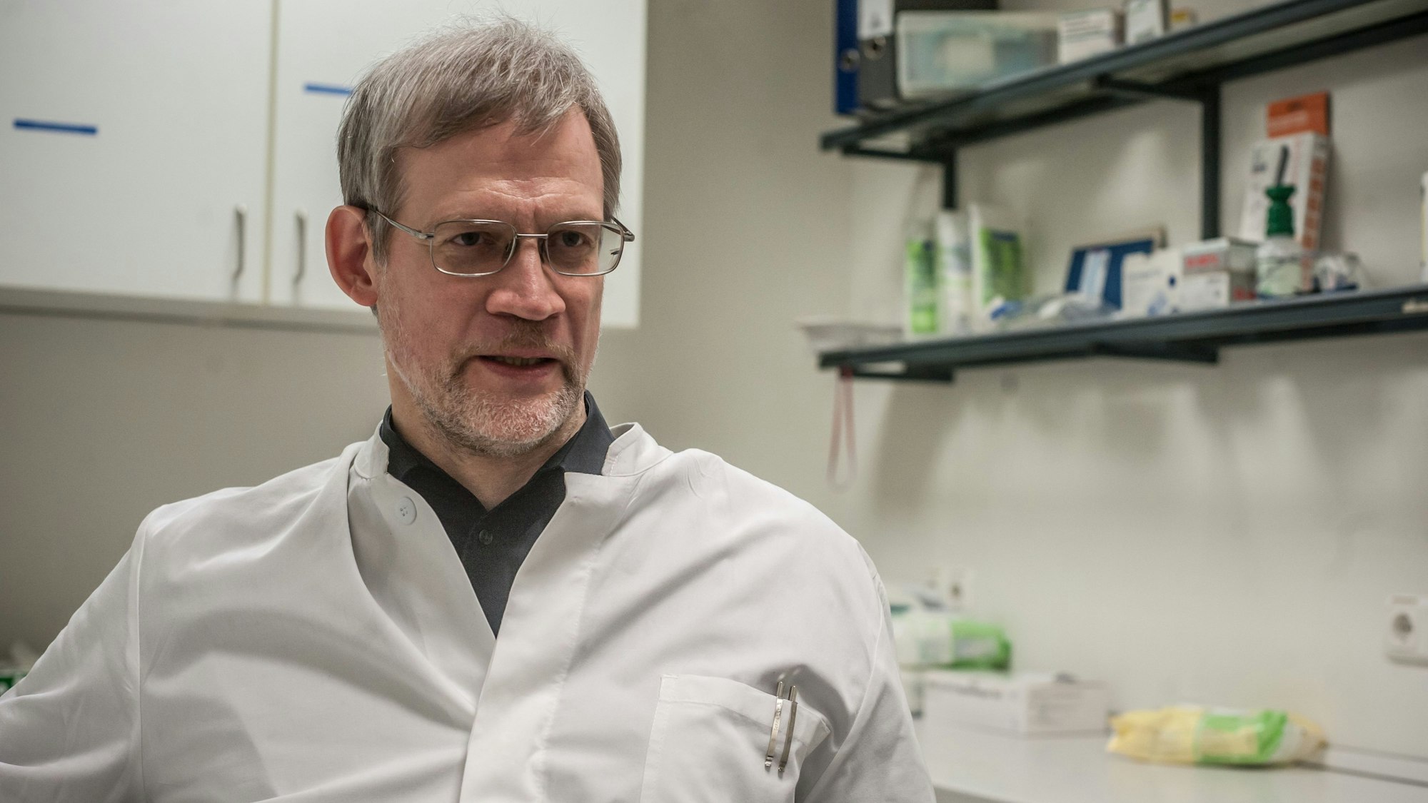 Martin Oehler in weißem Arztkittel mit Stiften in der Brusttasche in einem Behandlungszimmer oder Labor.
