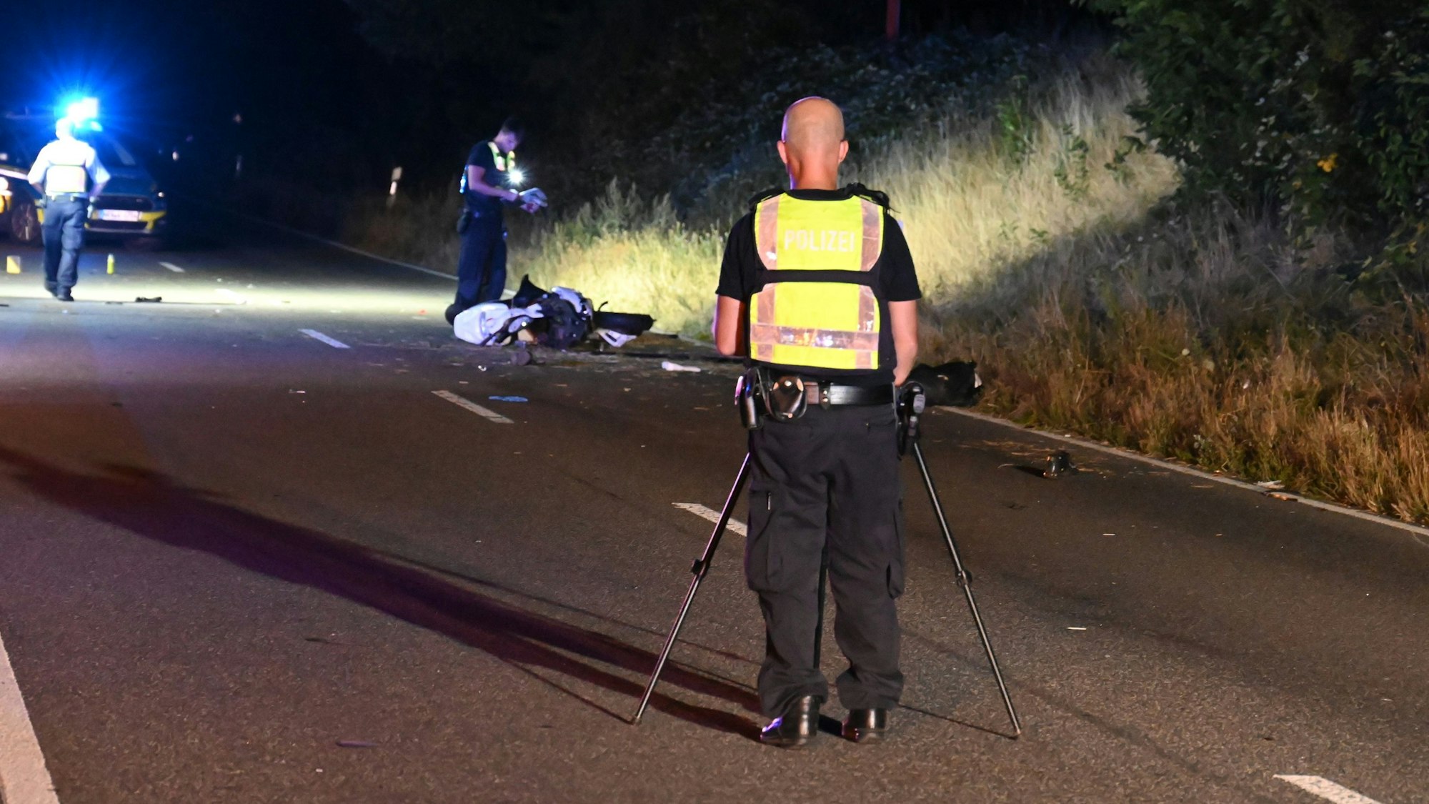 Polizisten sichernn Spuren an der Unfallstelle. Die B59 wird ausgeleuchtet, es ist Nacht.