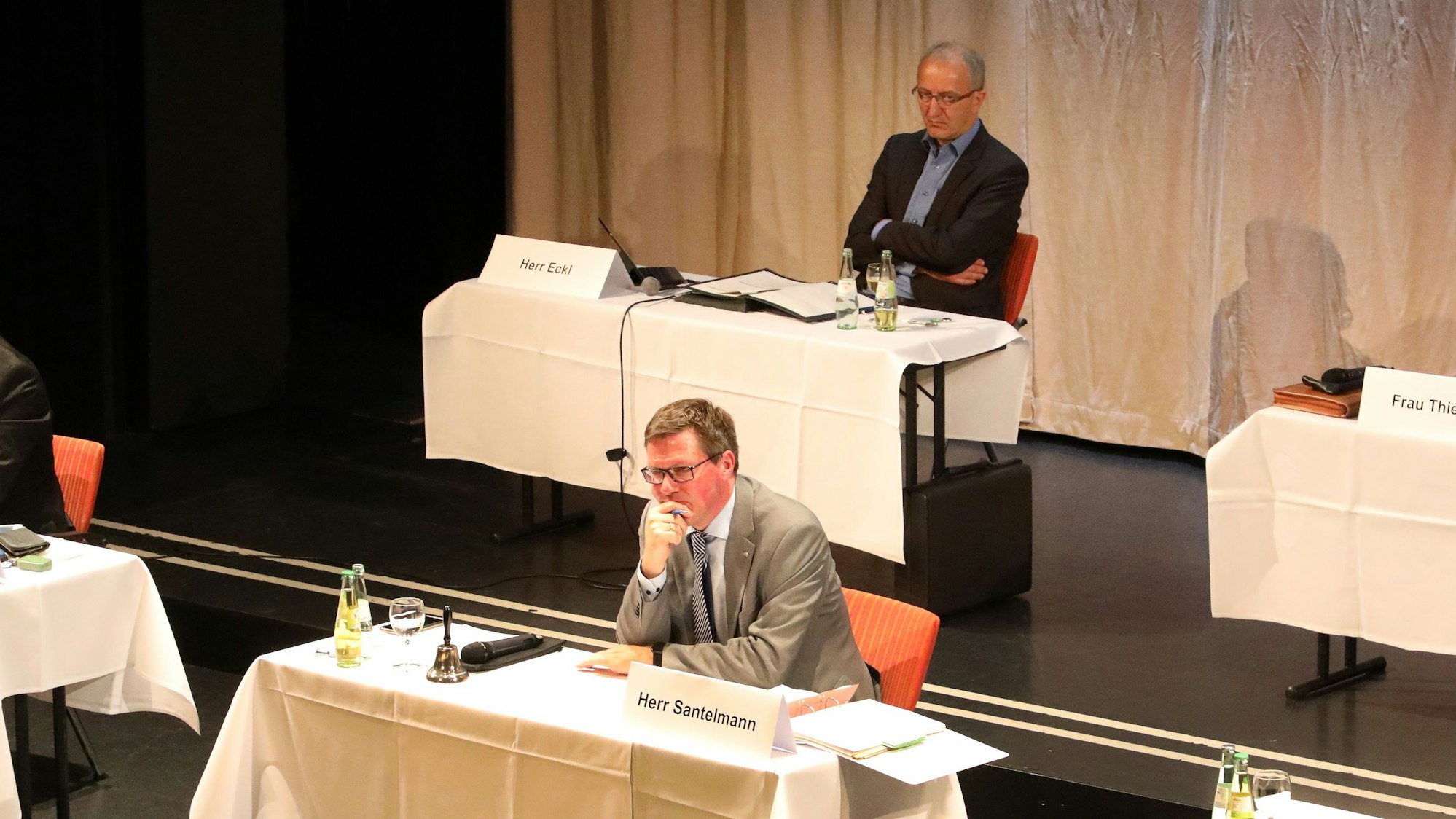 Landrat Stephan Santelmann und Kreiskämmerer Klaus Eckl sitzen an Podiums-Tischen in einem Saal.