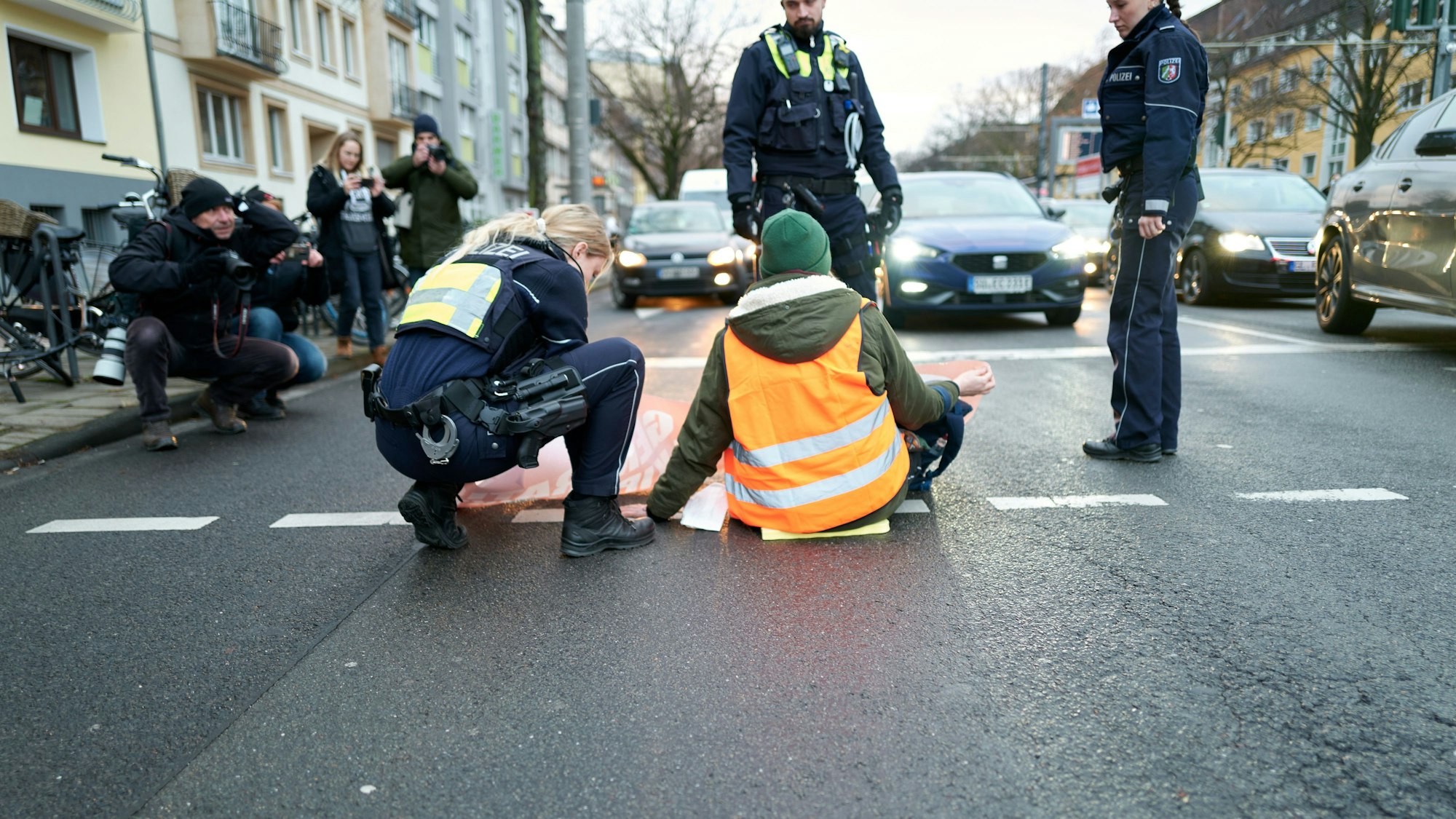 Aktivisten der „Letzten Generation“ kleben sich auf der Fahrbahn fest. Eine Polizistin überprüft, ob sie fest ist.