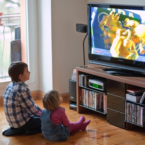 Zwei Kinder sitzen vor einem laufenden Fernseher auf dem Boden.