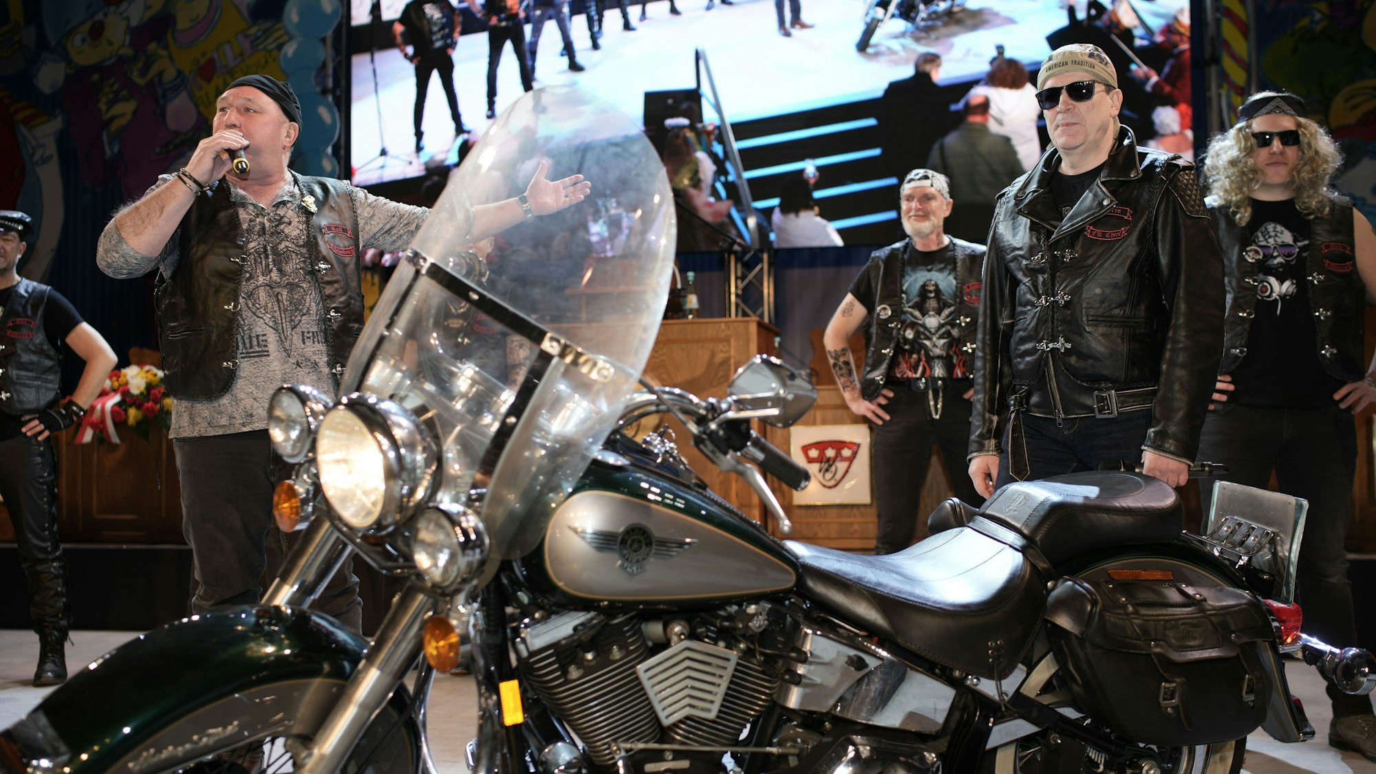 Bei der Mädchensitzung Willi-Ostermann-Gesellschaft kam der Elferrat als Rocker und Christoph Kuckelkorn (2.v.r.) mit Harley auf die Bühne. Präsident Ralph Schlegelmilch (l.) war begeistert. Alle Männer tragen Motorradkluft, im Vordergrund steht das Motorrad.
