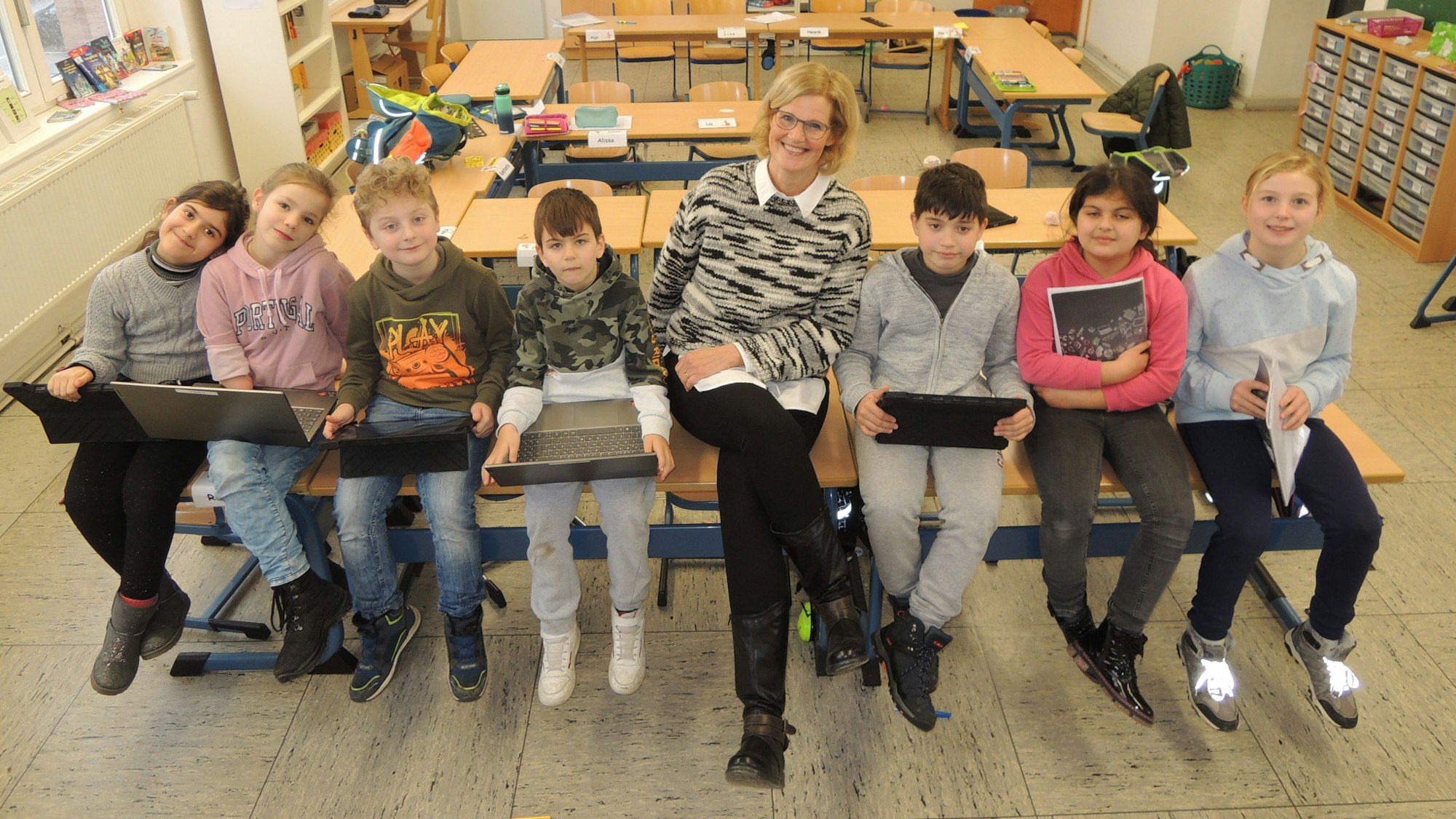Rektorin Tanja Claßen sitzt mit einigen Schülern und Schülerinnen in einer Klasse auf Tischen.