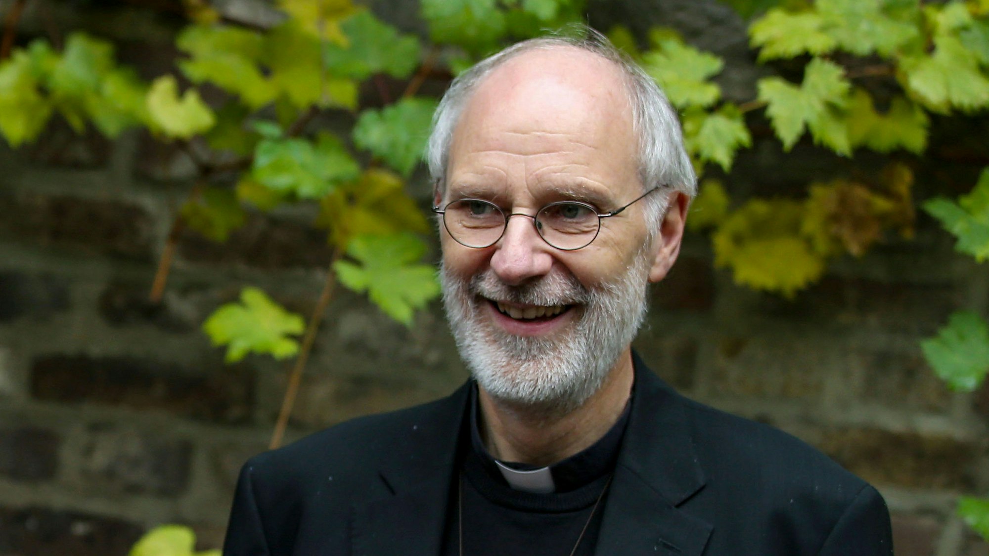 Weihbischof Ansgar Puff steht vor einer Mauer und lächelt.