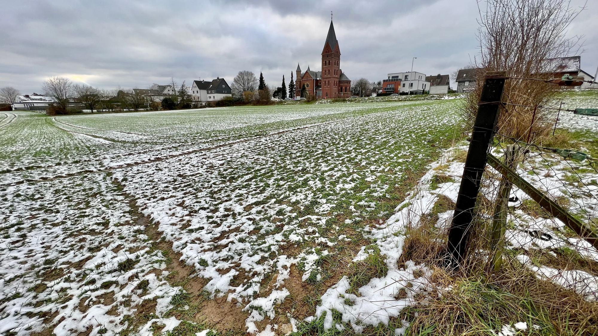 Feld mit etwas Schnee, im Hintergrund die Kirche von Neuboddenberg und Häuser