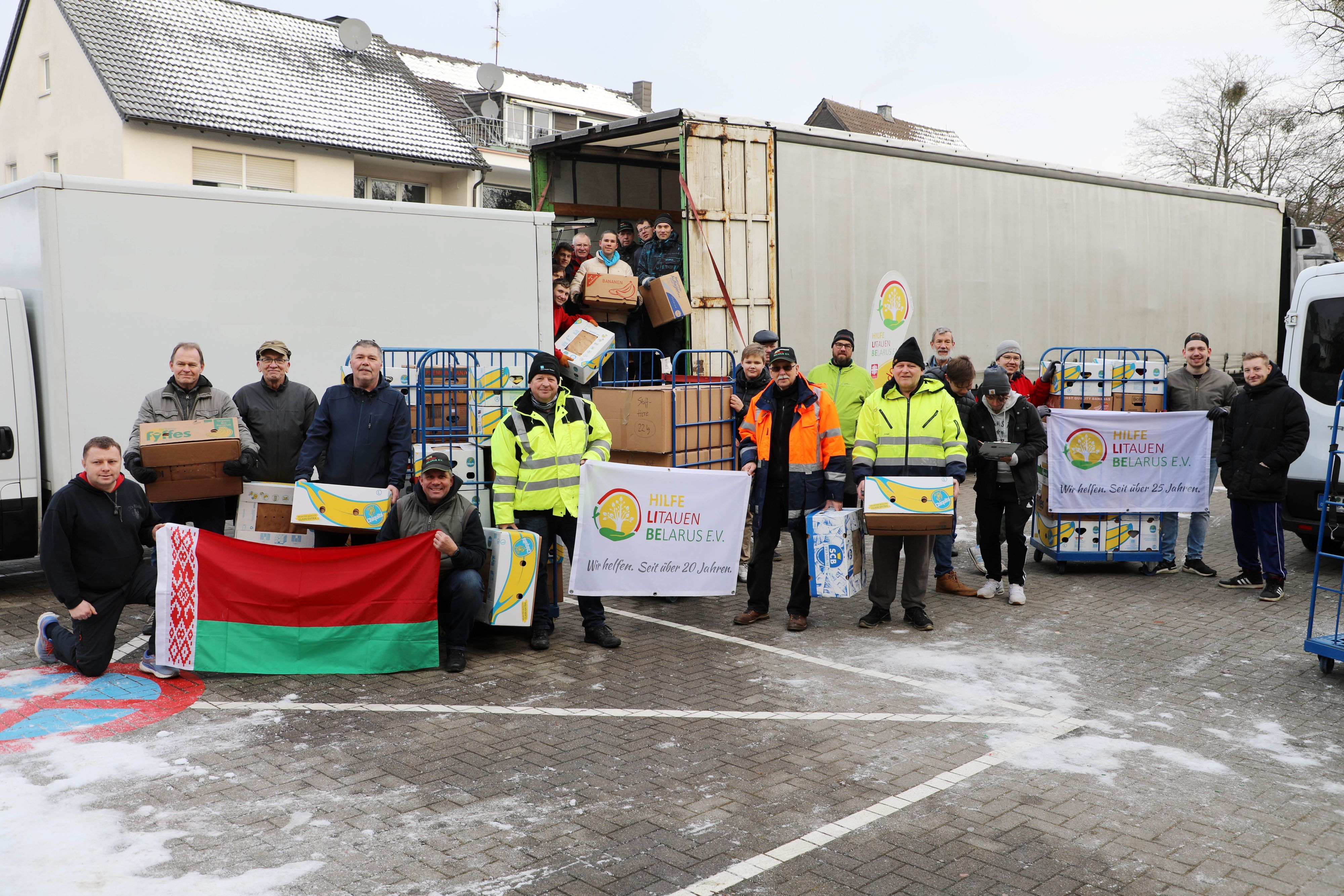 Helfer stehen mit der Fahne von Belarus und des Vereins Hilfe Litauen Belarus vor einem Lkw, der beladen wird.