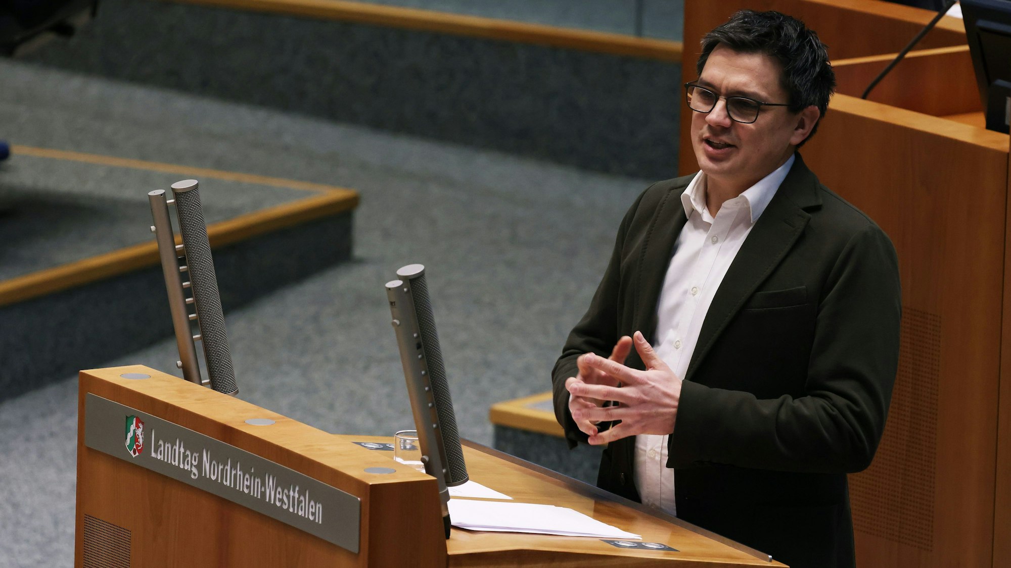Alexander Vogt von der SPD steht im Landtag am Rednerpult und spricht. Seine Finger hält er vor sich zusammengelegt, er trägt einen dunklen Anzug ohne Krawatte und ein weißes Hemd.
