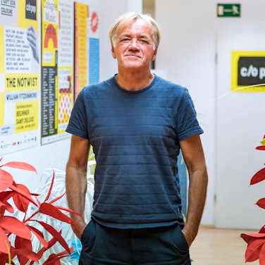 Norbert Oberhaus steht in einem Flur vor Blumen und Postern und schaut in die Kamera.