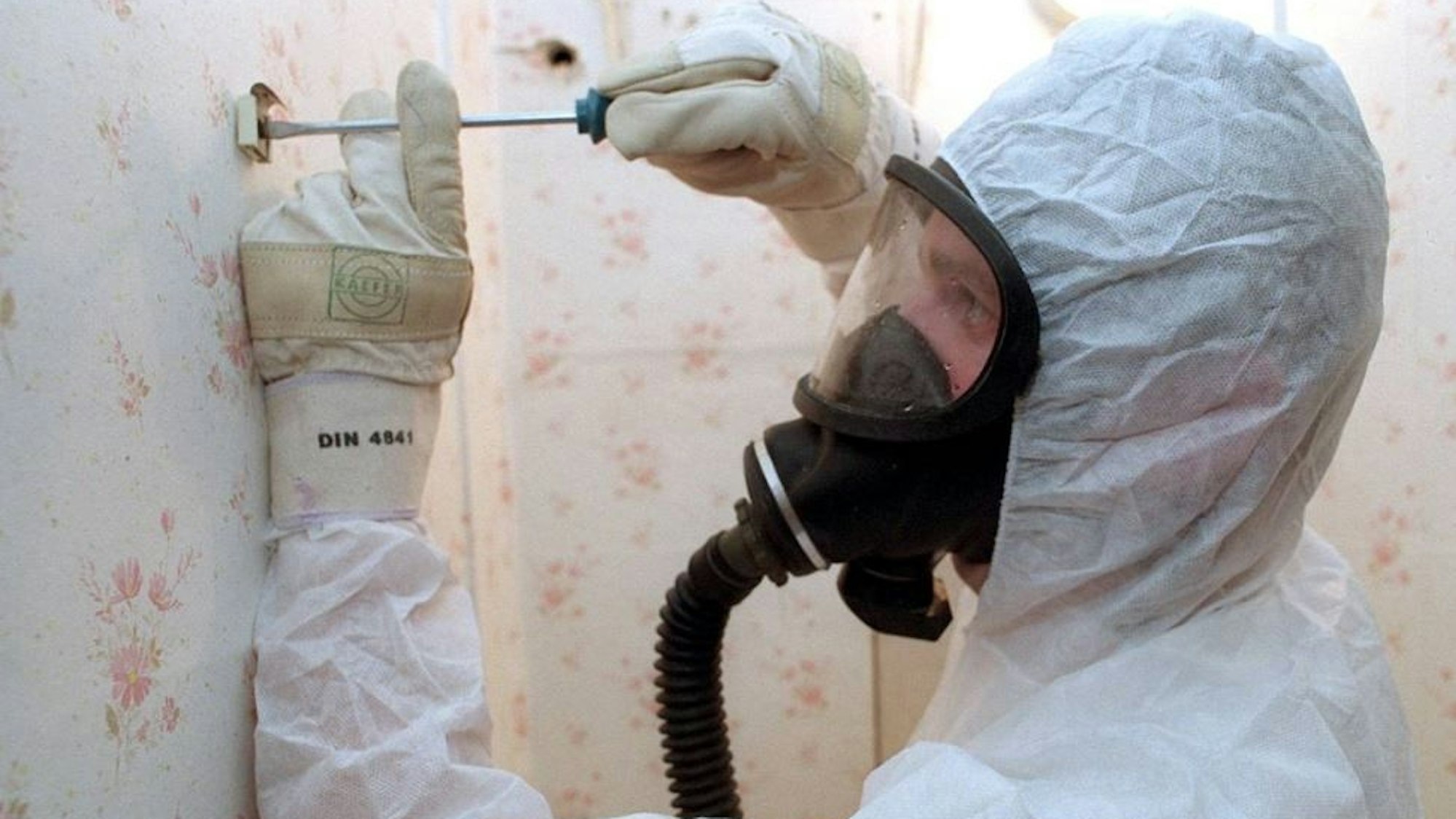 Ein Arbeiter im Overall mit Atemmaske saniert eine Wand.