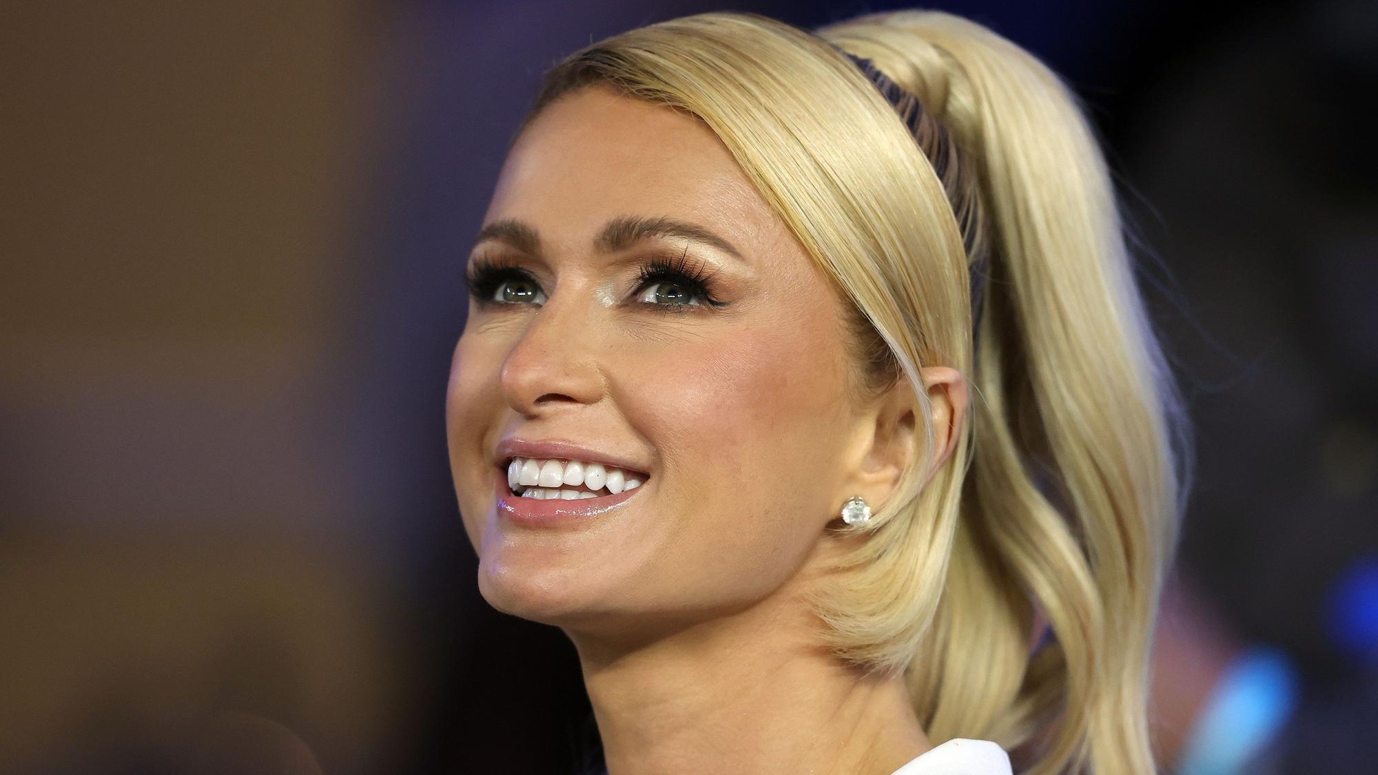 Paris Hilton lacht freundlich an der Kamera vorbei.